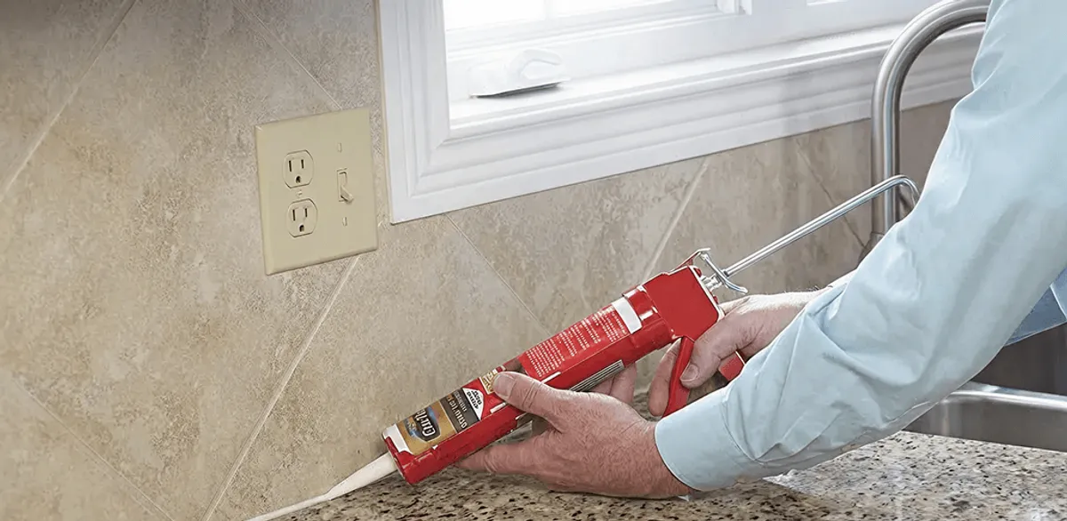 Handyman applying caulk along a kitchen backsplash and countertop seam in Knoxville, TN